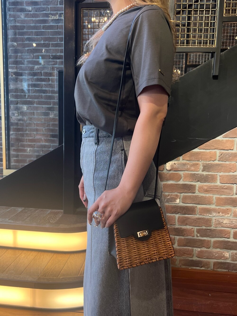 グレー系のデニムスカート、ブラック系のショルダーバッグ、グレー系のTシャツ/カットソーを着用したレディースの夏コーディネートの3枚目の写真