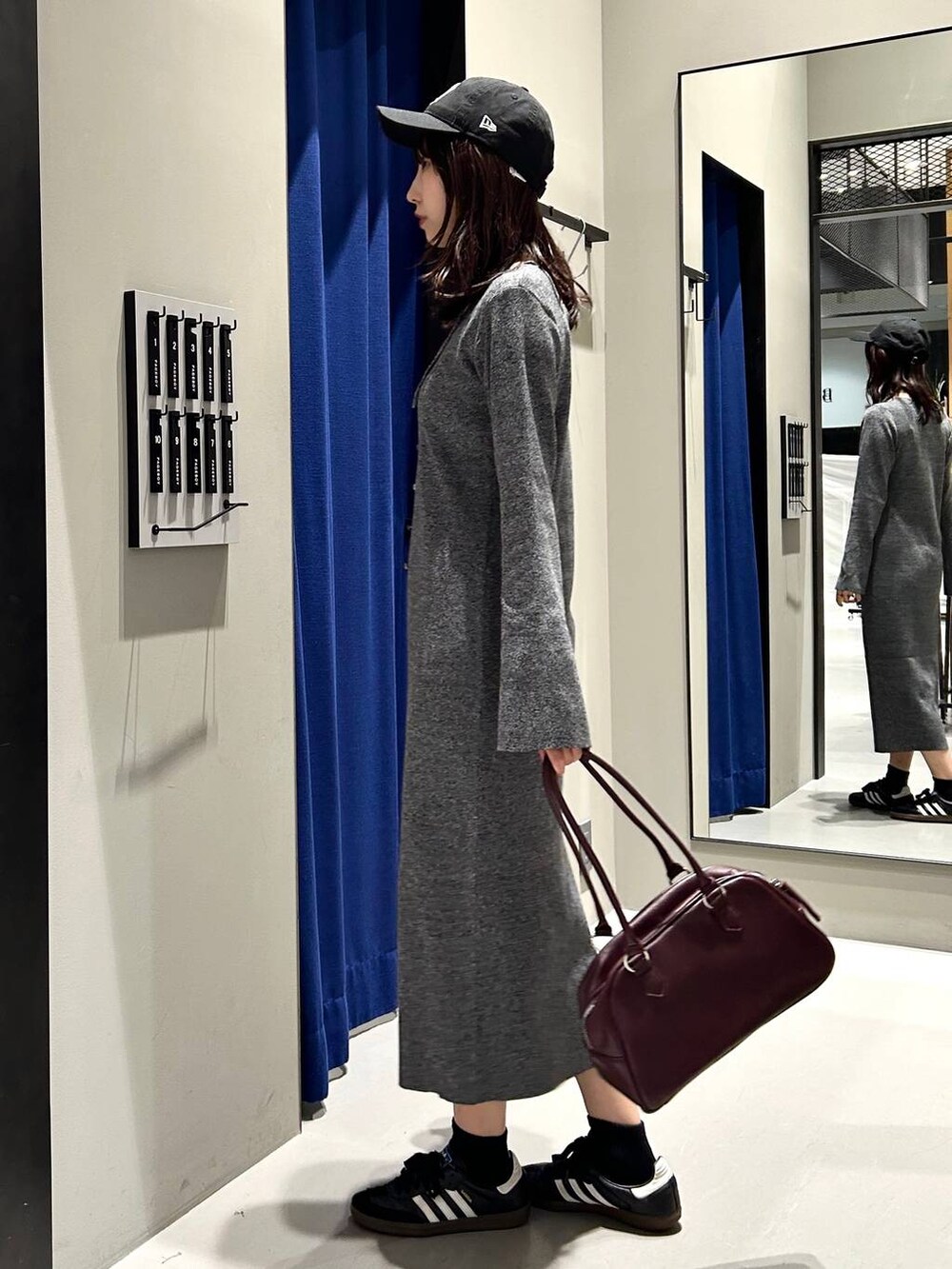 グレー系のワンピース、レッド系のボストンバッグ、ブラック系のキャップを着用したレディースの秋コーディネートの5枚目の写真