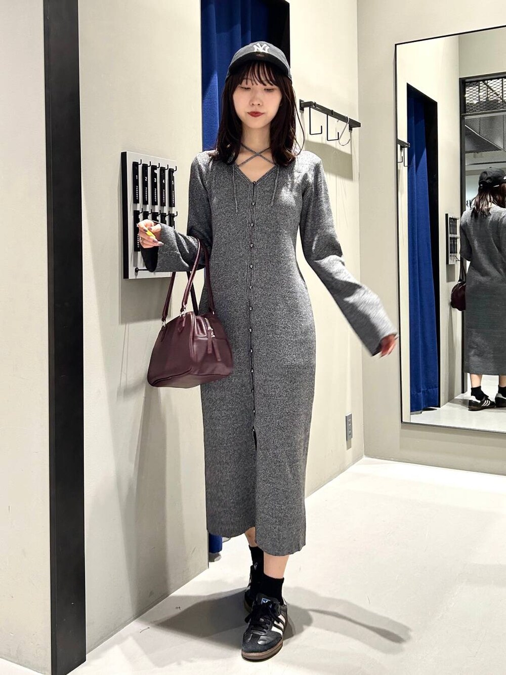 グレー系のワンピース、レッド系のボストンバッグ、ブラック系のキャップを着用したレディースの秋コーディネートの4枚目の写真