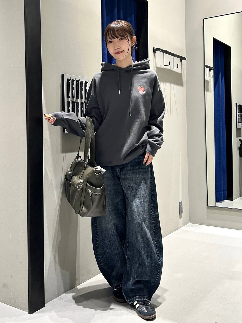 グリーン系のボストンバッグ、グレー系のパーカー、ブルー系のデニムパンツを着用したレディースの秋コーディネートの2枚目の写真