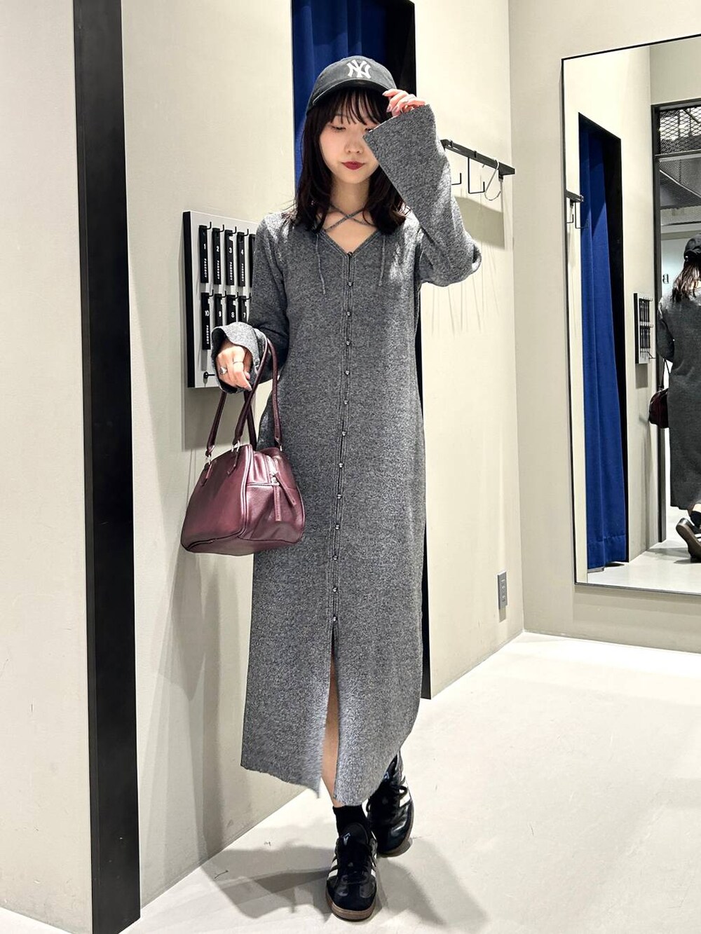 グレー系のワンピース、レッド系のボストンバッグ、ブラック系のキャップを着用したレディースの秋コーディネートの2枚目の写真