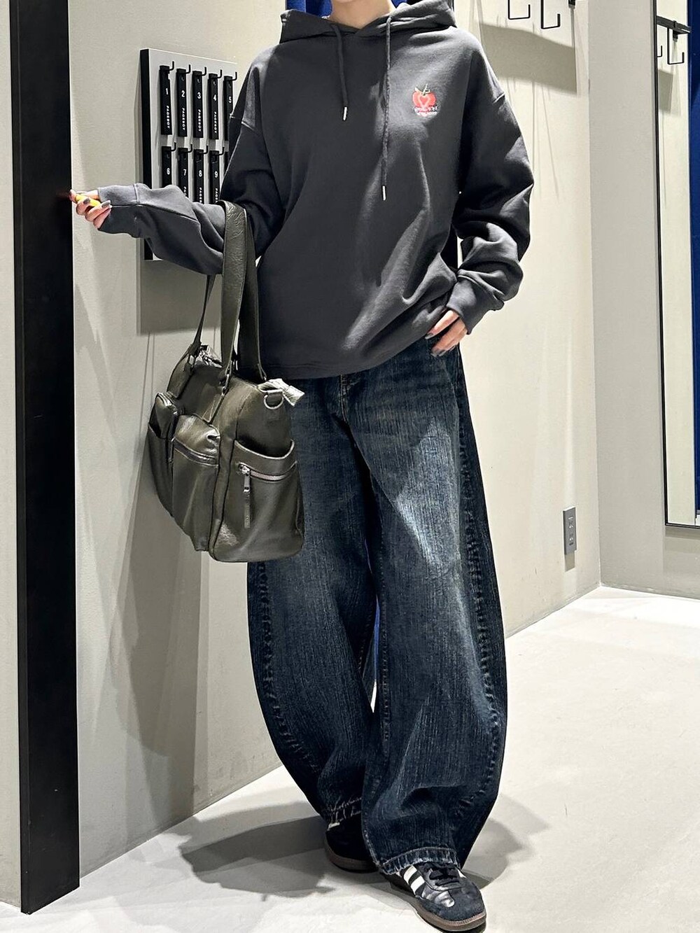 グリーン系のボストンバッグ、グレー系のパーカー、ブルー系のデニムパンツを着用したレディースの秋コーディネートの5枚目の写真