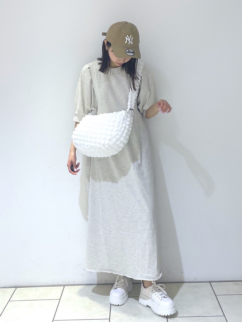 ベージュ系のワンピース、ホワイト系のバッグ、ホワイト系のスニーカーを着用したレディースの春コーディネートの2枚目の写真