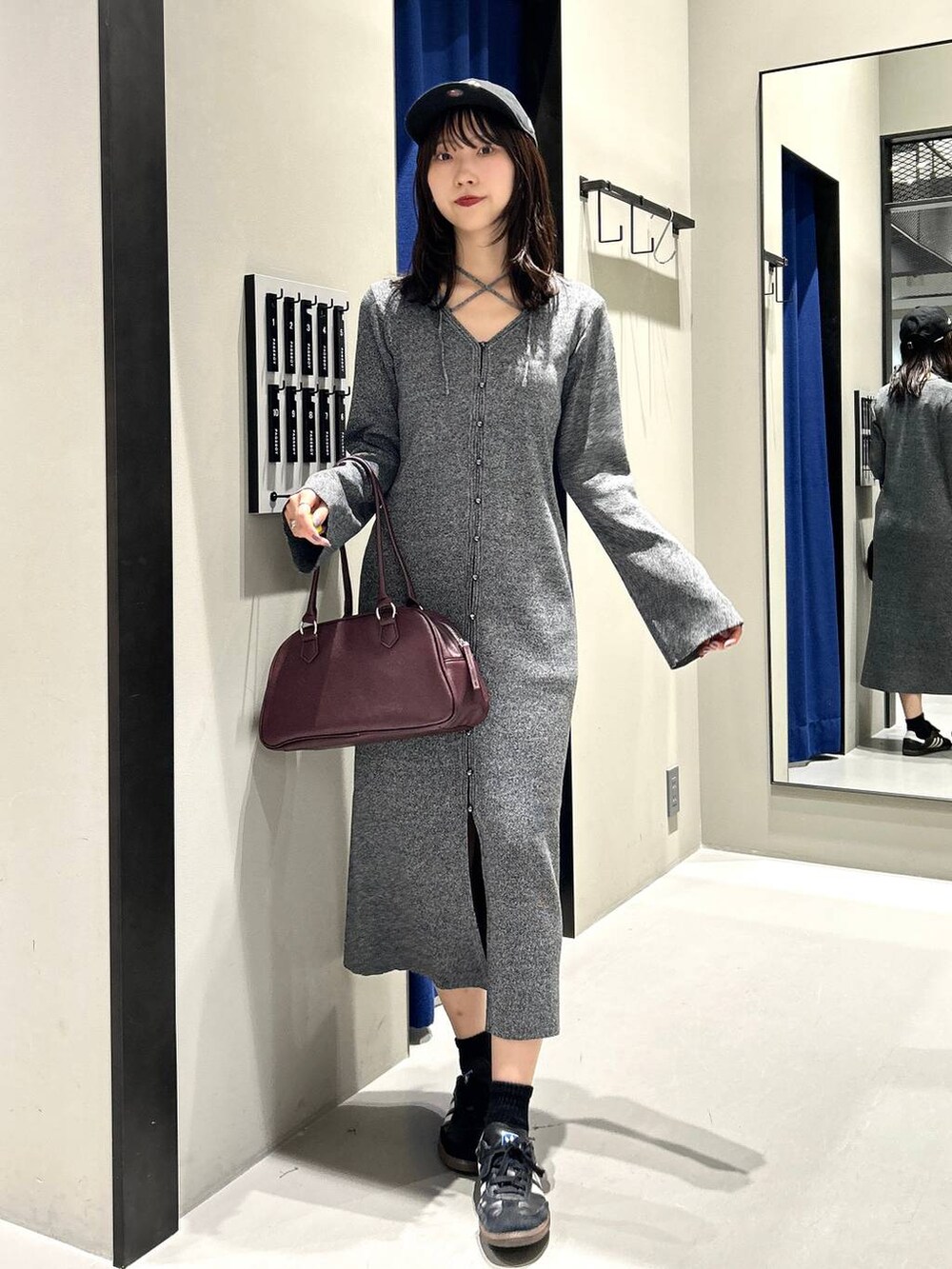 グレー系のワンピース、レッド系のボストンバッグ、ブラック系のキャップを着用したレディースの秋コーディネートの3枚目の写真