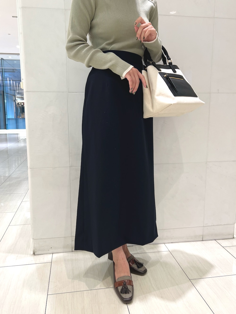 グリーン系のニット/セーター、ブルー系のスカート、ブラウン系のパンプスを着用したレディースの秋コーディネートの3枚目の写真