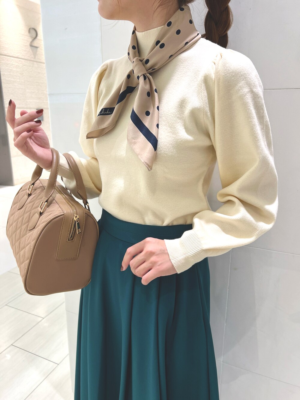 ホワイト系のニット/セーター、グリーン系のスカート、ベージュ系のハンドバッグを着用したレディースの秋コーディネートの2枚目の写真