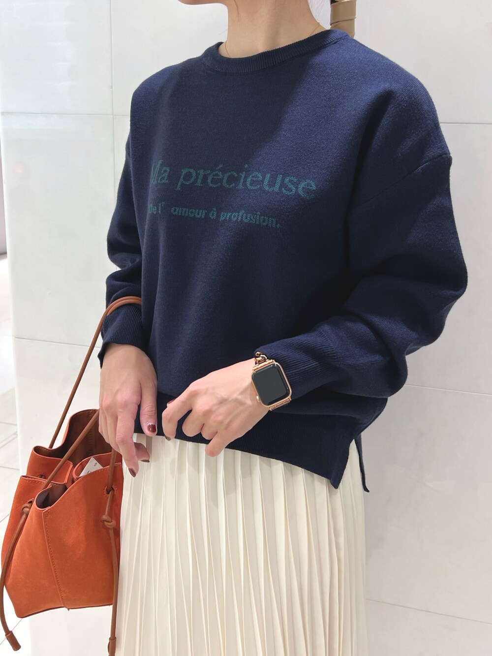 ブルー系のニット/セーター、ホワイト系のスカート、オレンジ系のハンドバッグを着用したレディースの秋コーディネートの2枚目の写真