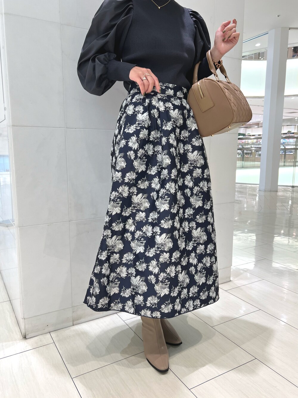 グレー系のニット/セーター、ブルー系のスカート、ベージュ系のハンドバッグを着用したレディースの秋コーディネートの4枚目の写真