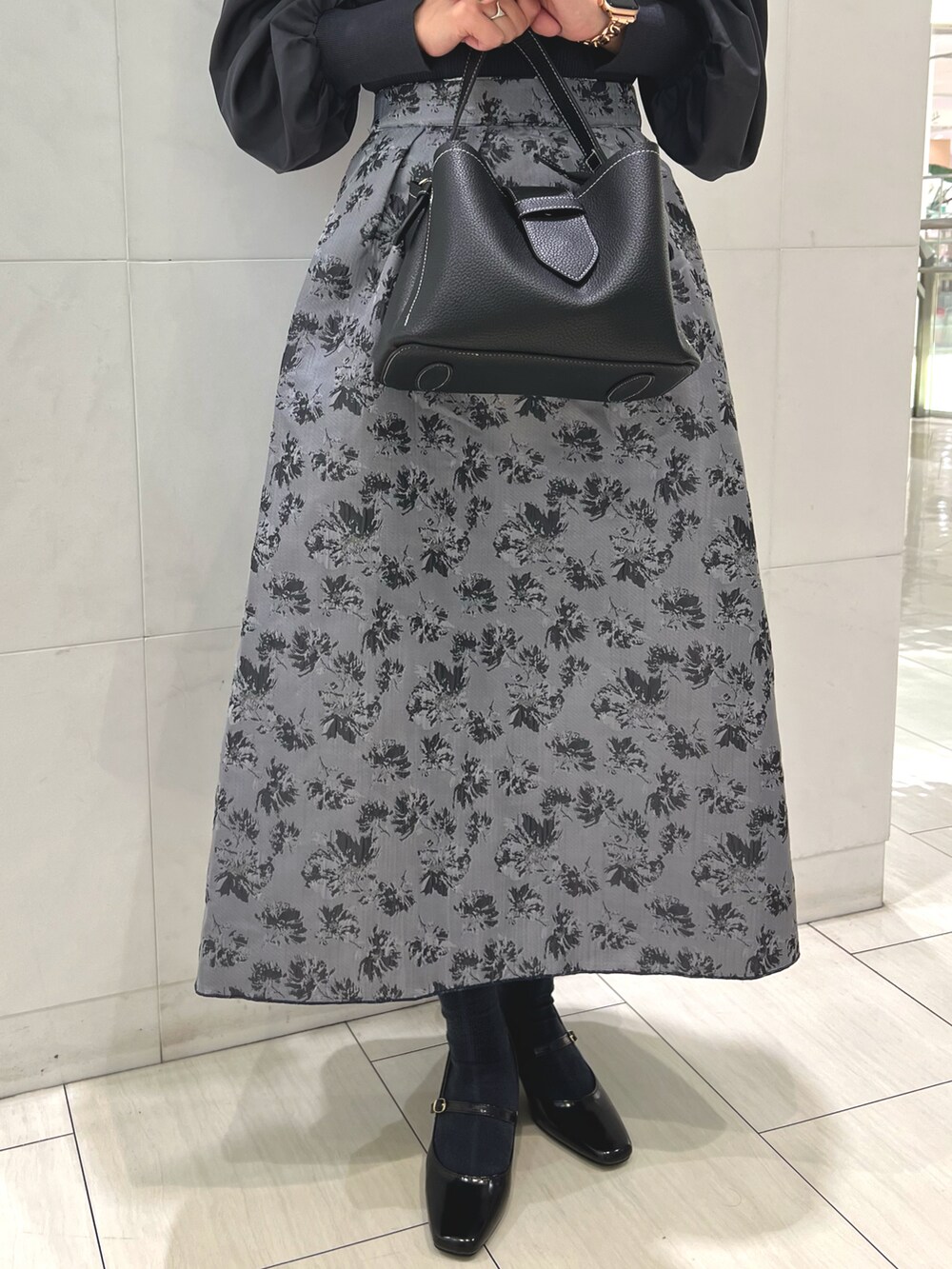 グレー系のニット/セーター、ブラック系のハンドバッグ、ブラック系のパンプスを着用したレディースの秋コーディネートの4枚目の写真