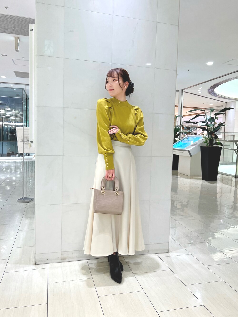 ブラック系のブーツ、ベージュ系のチェスターコート、イエロー系のニット/セーターを着用したレディースの秋コーディネートの2枚目の写真