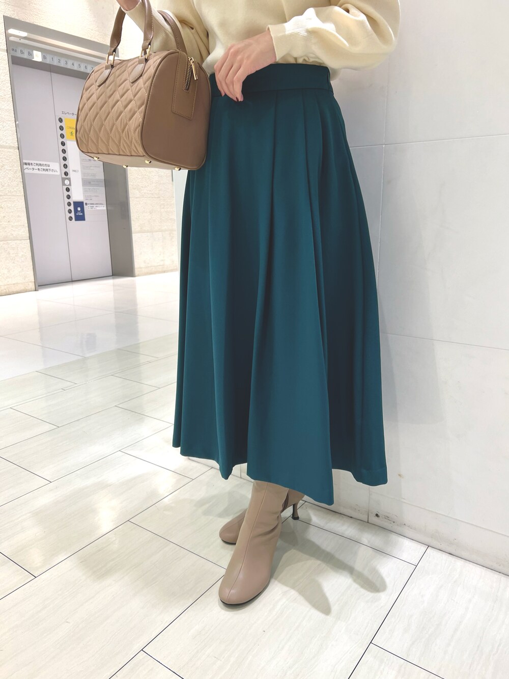 ホワイト系のニット/セーター、グリーン系のスカート、ベージュ系のハンドバッグを着用したレディースの秋コーディネートの3枚目の写真