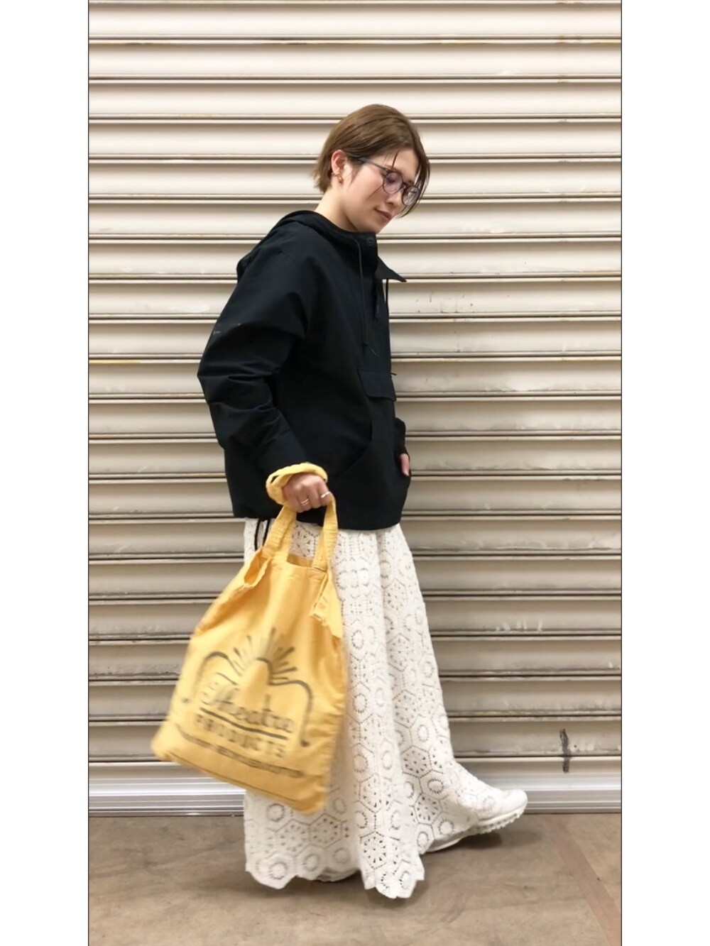 イエロー系のトートバッグ、ブラック系のパーカー、ホワイト系のスカートを着用したレディースの春コーディネートの2枚目の写真