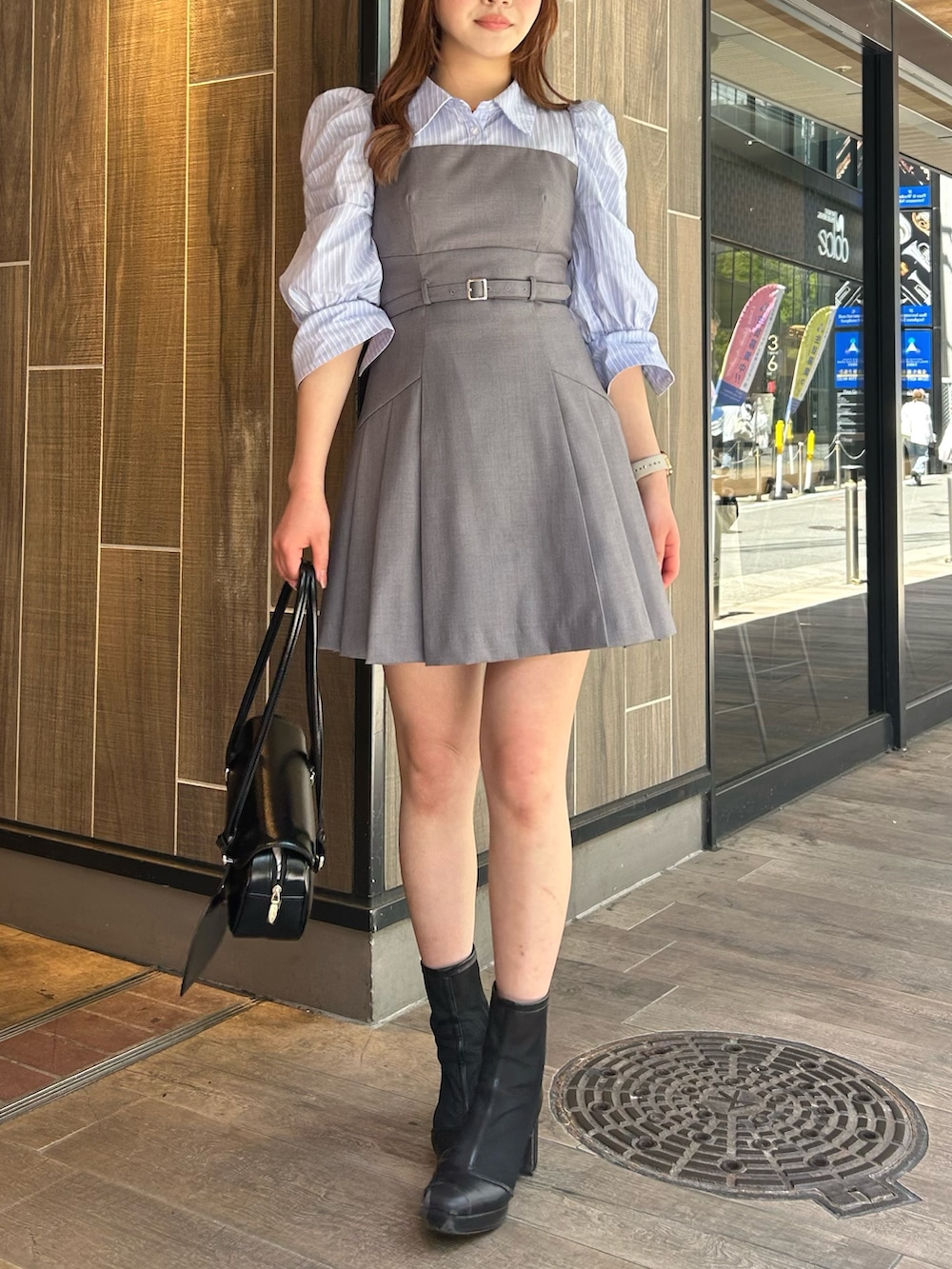 グレー系のワンピース、ブラック系のハンドバッグ、ブラック系のブーツを着用したレディースの春コーディネートの2枚目の写真