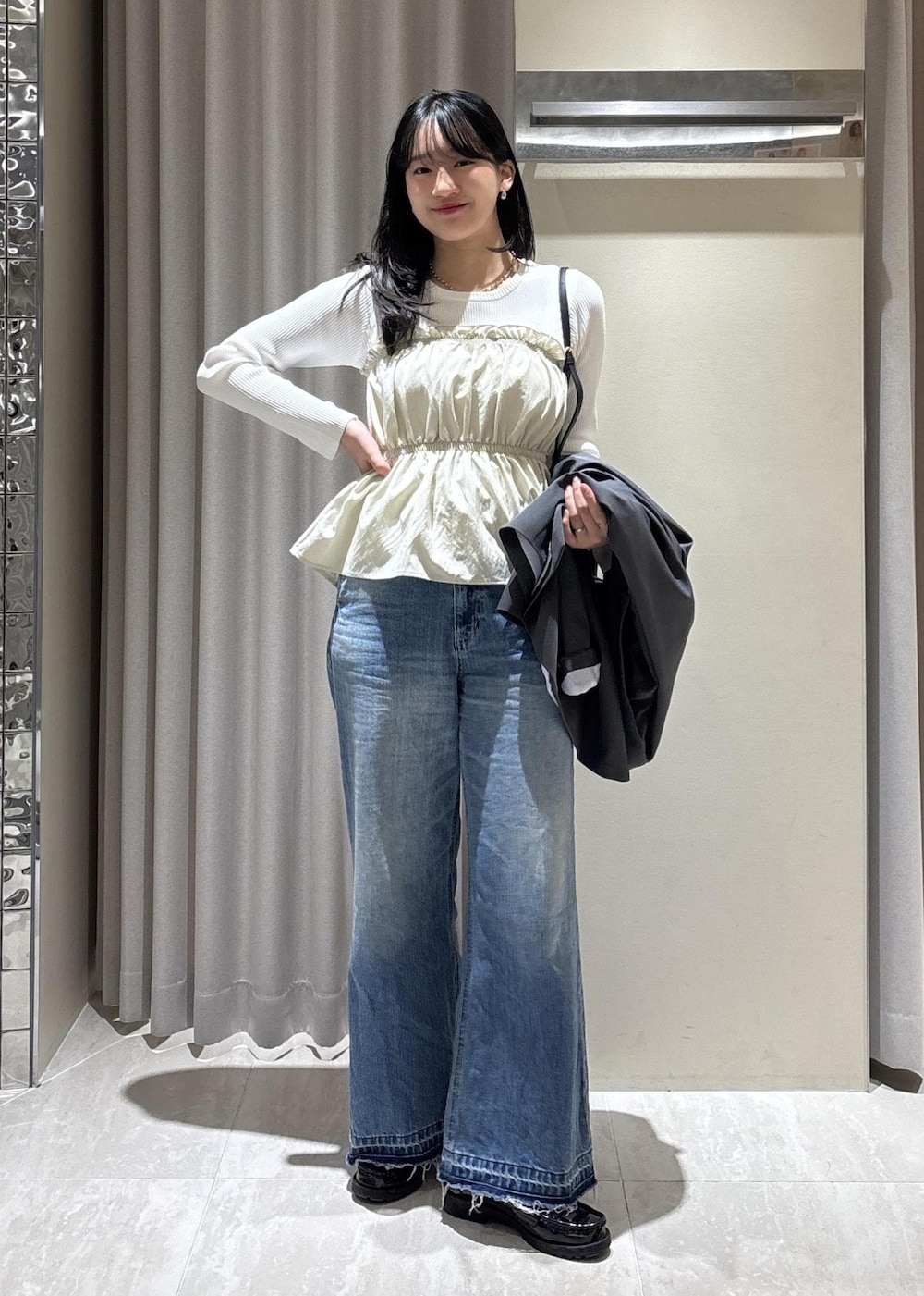 ブラック系のショルダーバッグ、ブルー系のデニムパンツ、ホワイト系のニット/セーターを着用したレディースの春コーディネートの2枚目の写真