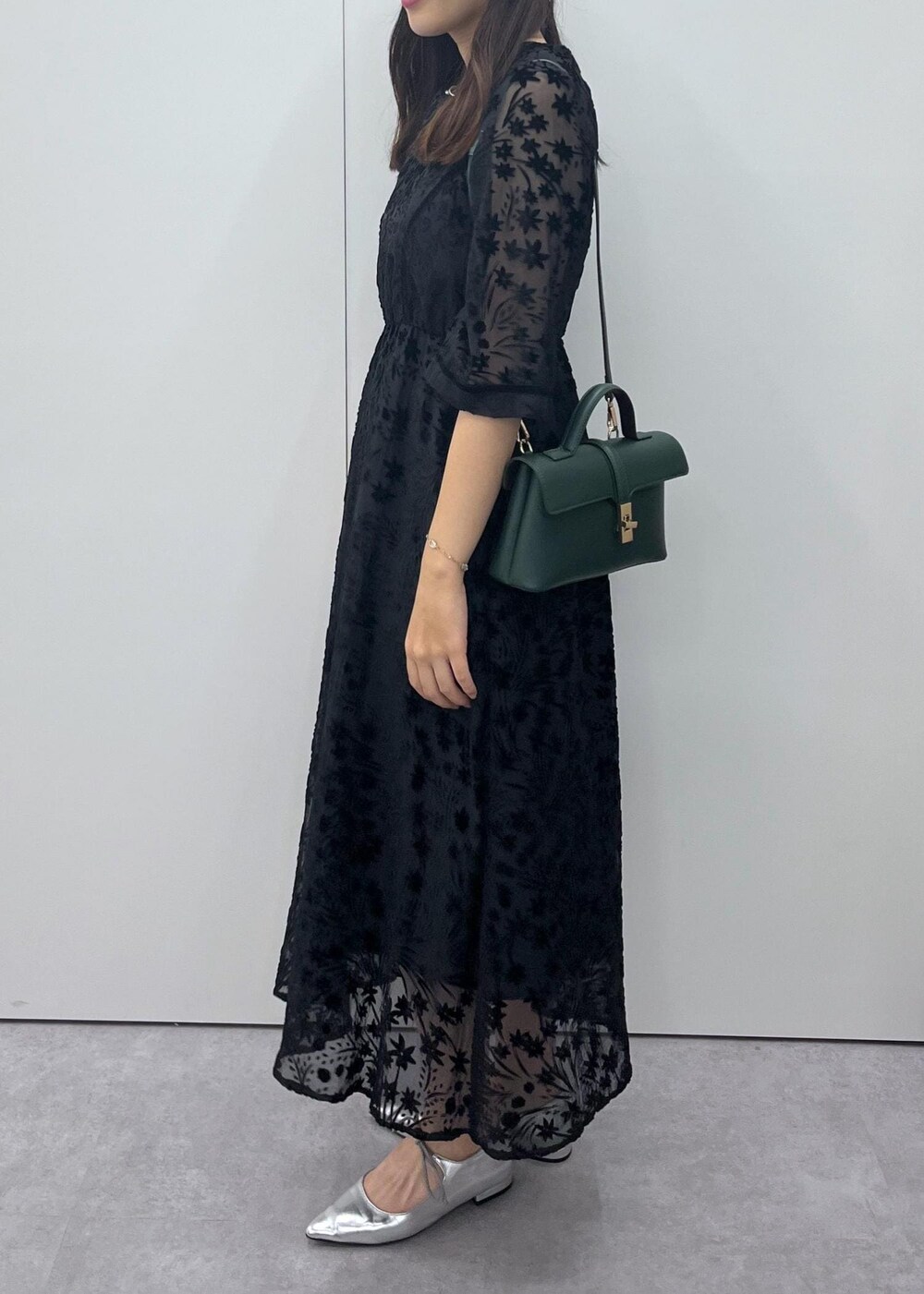 シルバー系のパンプス、グリーン系のショルダーバッグ、ブラック系のドレスを着用したレディースの秋コーディネートの2枚目の写真