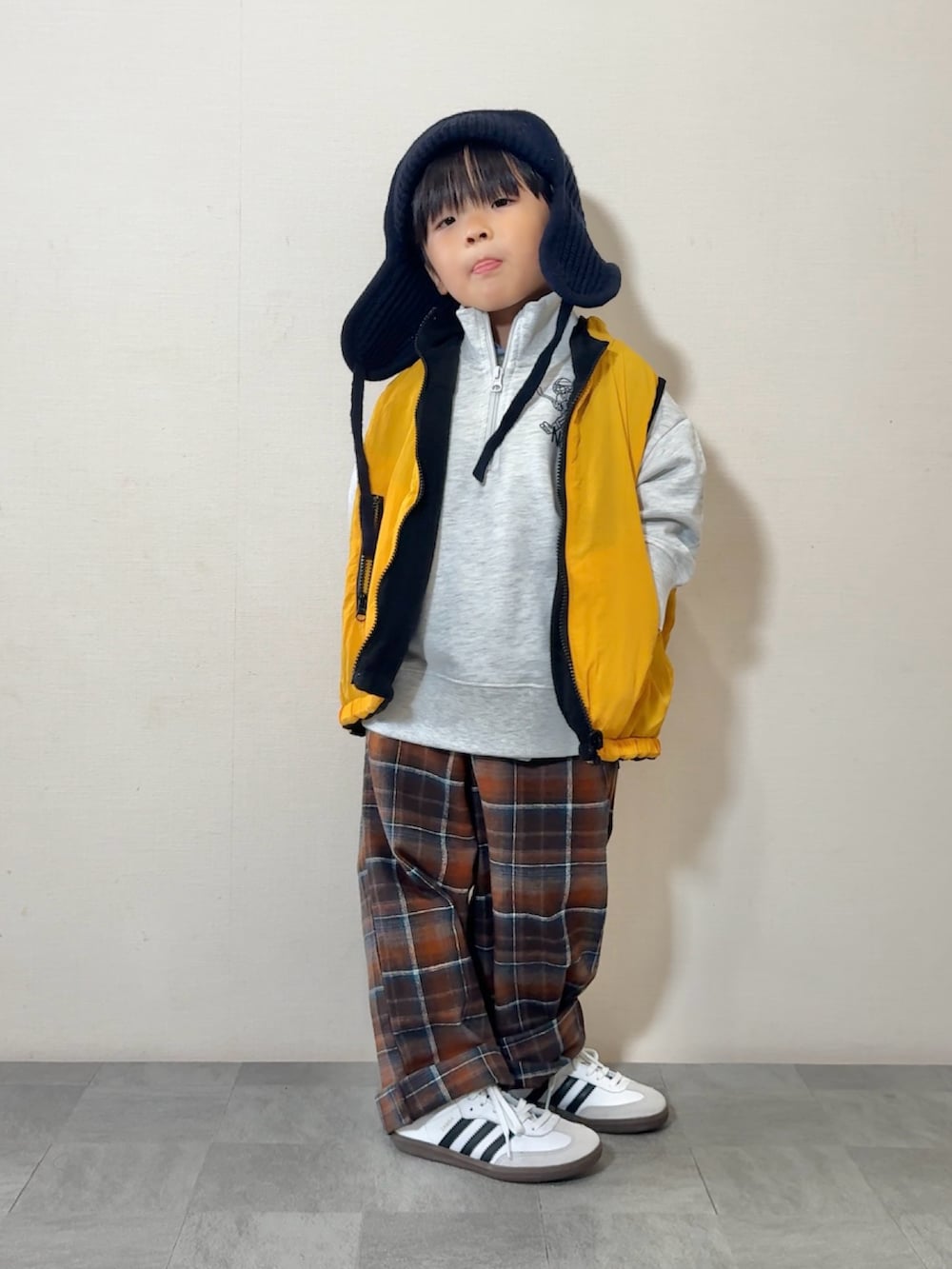 イエロー系のベスト、ホワイト系のスニーカー、グレー系のスウェットを着用したキッズの秋コーディネートの2枚目の写真
