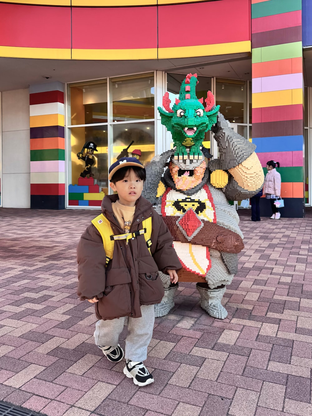 ブラウン系のダウンジャケット/コート、グレー系のスウェットパンツ、イエロー系のバックパック/リュックを着用したキッズの冬コーディネートの3枚目の写真