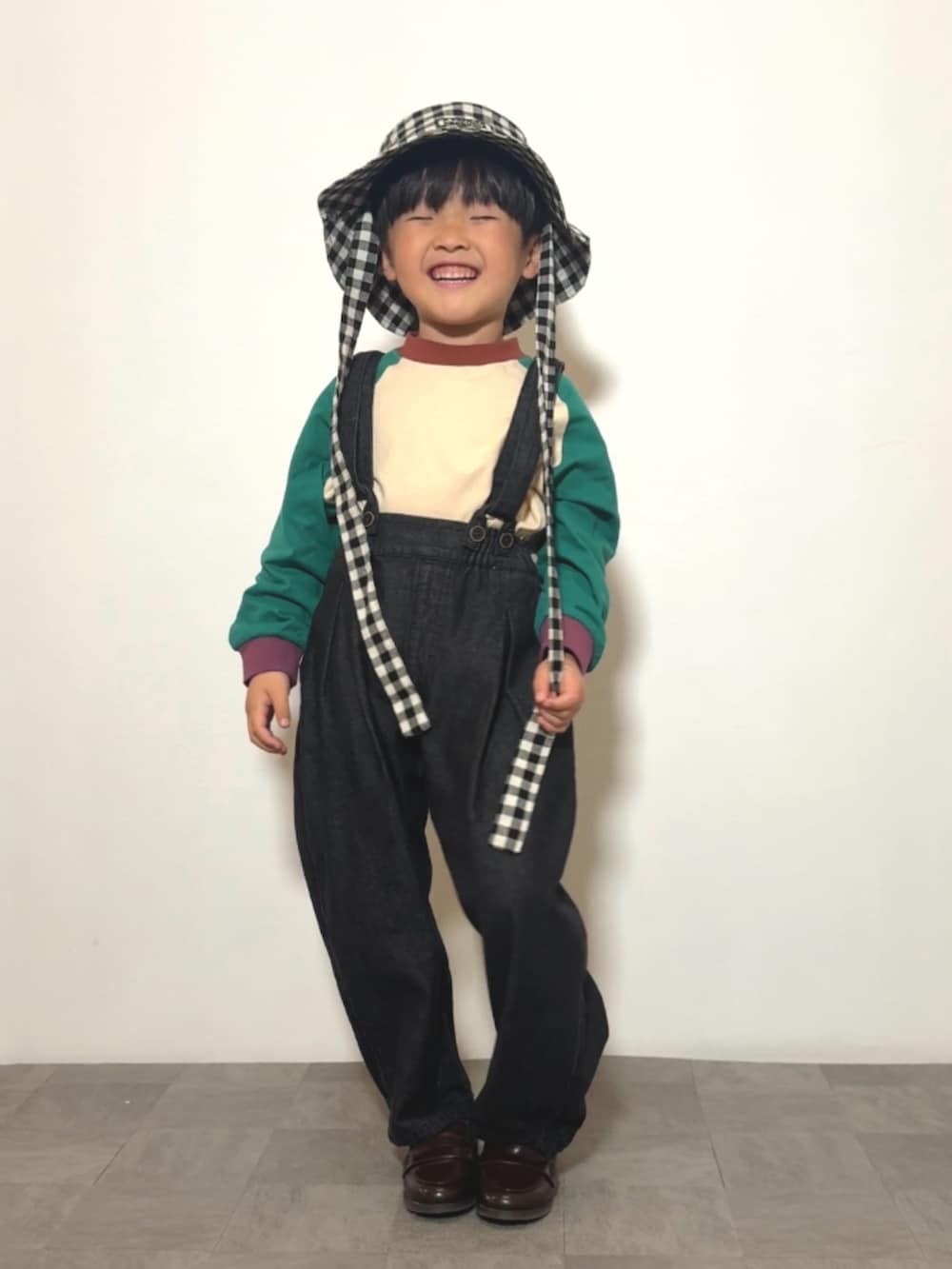 ブラック系のサロペット/オーバーオール、ブラウン系のローファー、グリーン系のTシャツ/カットソーを着用したキッズの春コーディネートの2枚目の写真