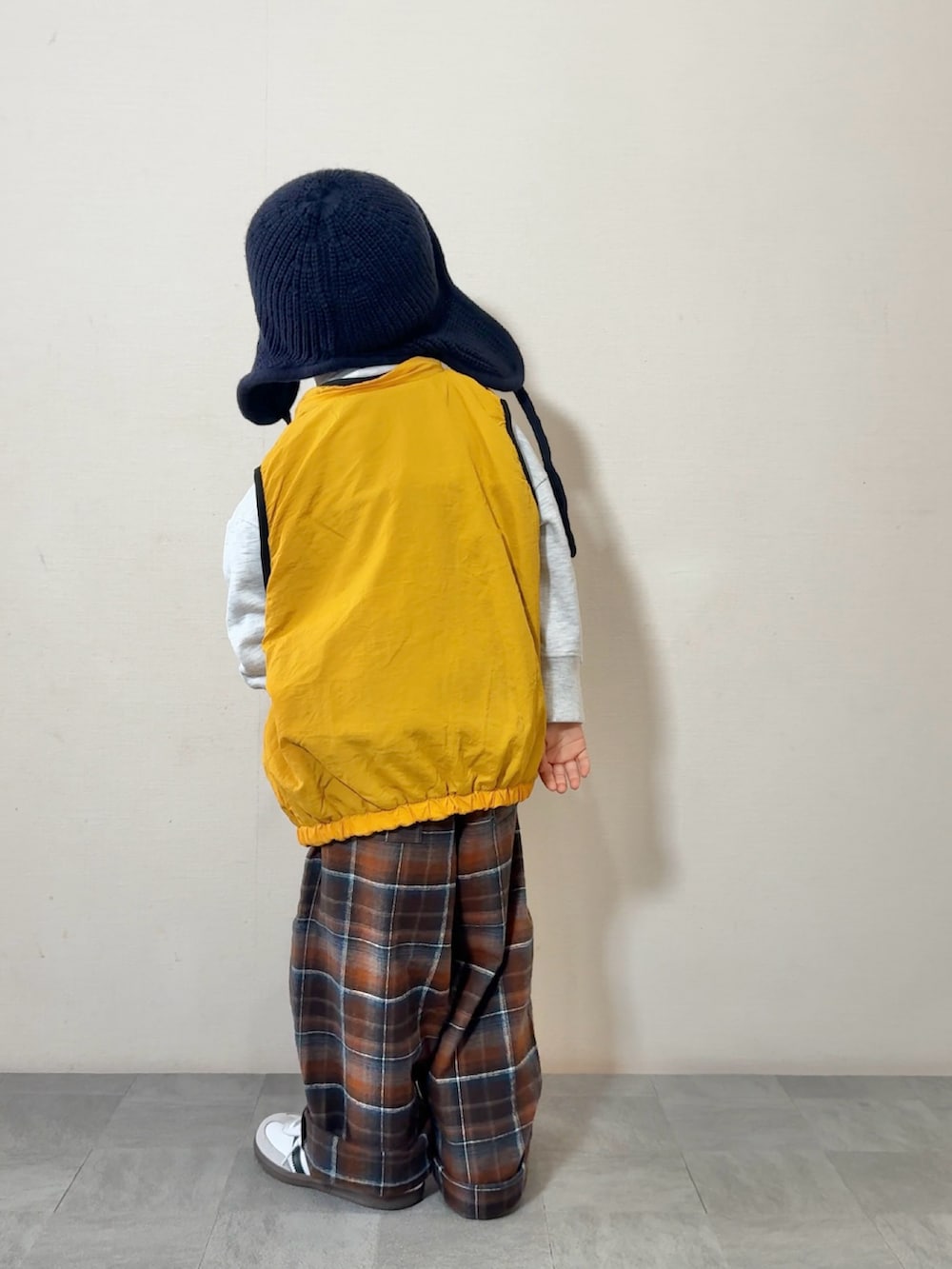 イエロー系のベスト、ホワイト系のスニーカー、グレー系のスウェットを着用したキッズの秋コーディネートの4枚目の写真