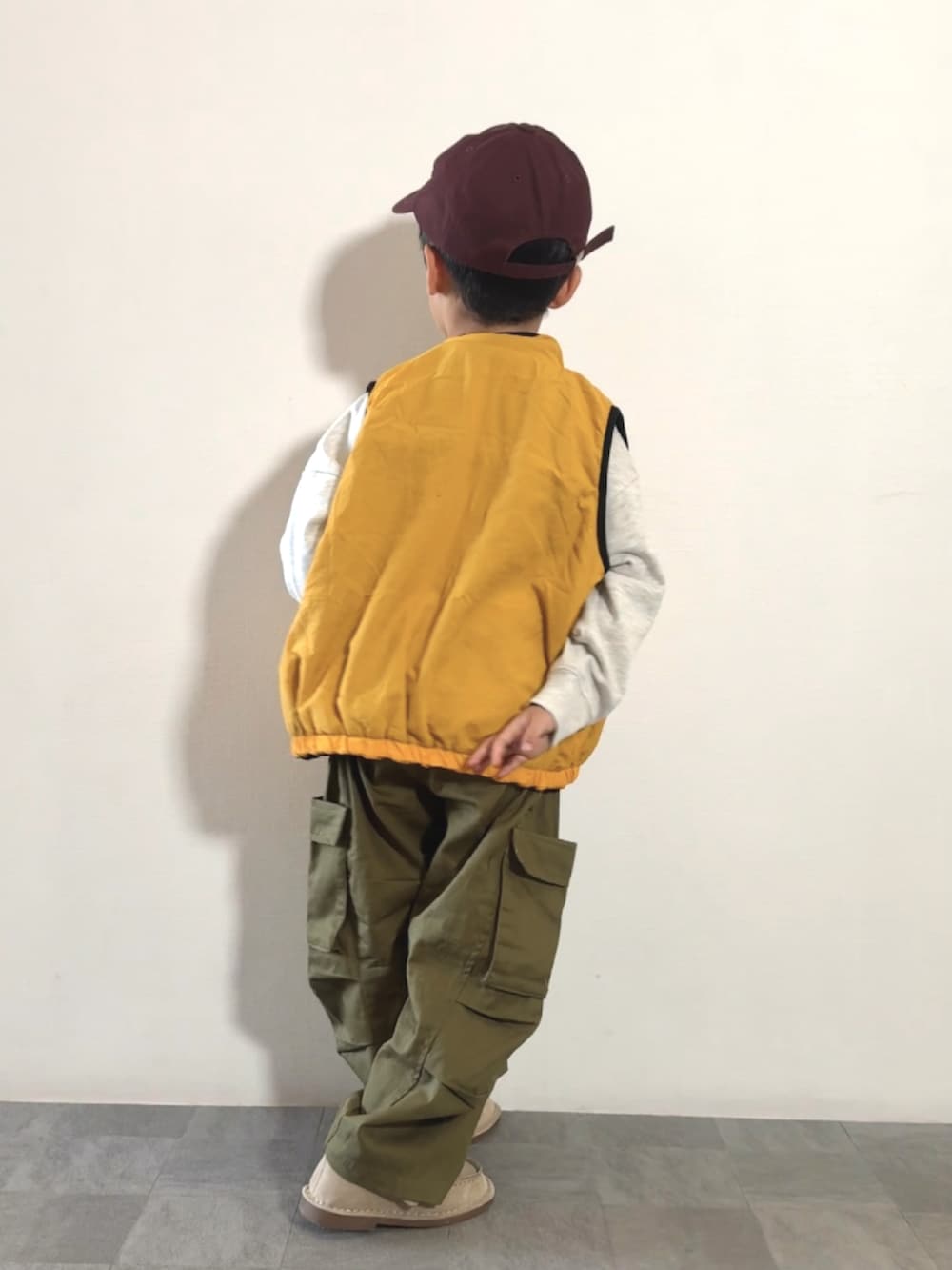 イエロー系のベスト、ベージュ系のモカシン/デッキシューズ、グリーン系のカーゴパンツを着用したキッズの秋コーディネートの3枚目の写真