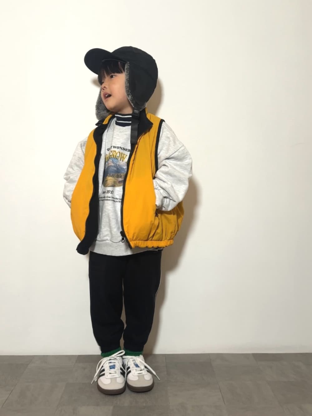 イエロー系のベスト、ブラック系のスウェットパンツ、ホワイト系のスニーカーを着用したキッズの冬コーディネートの2枚目の写真