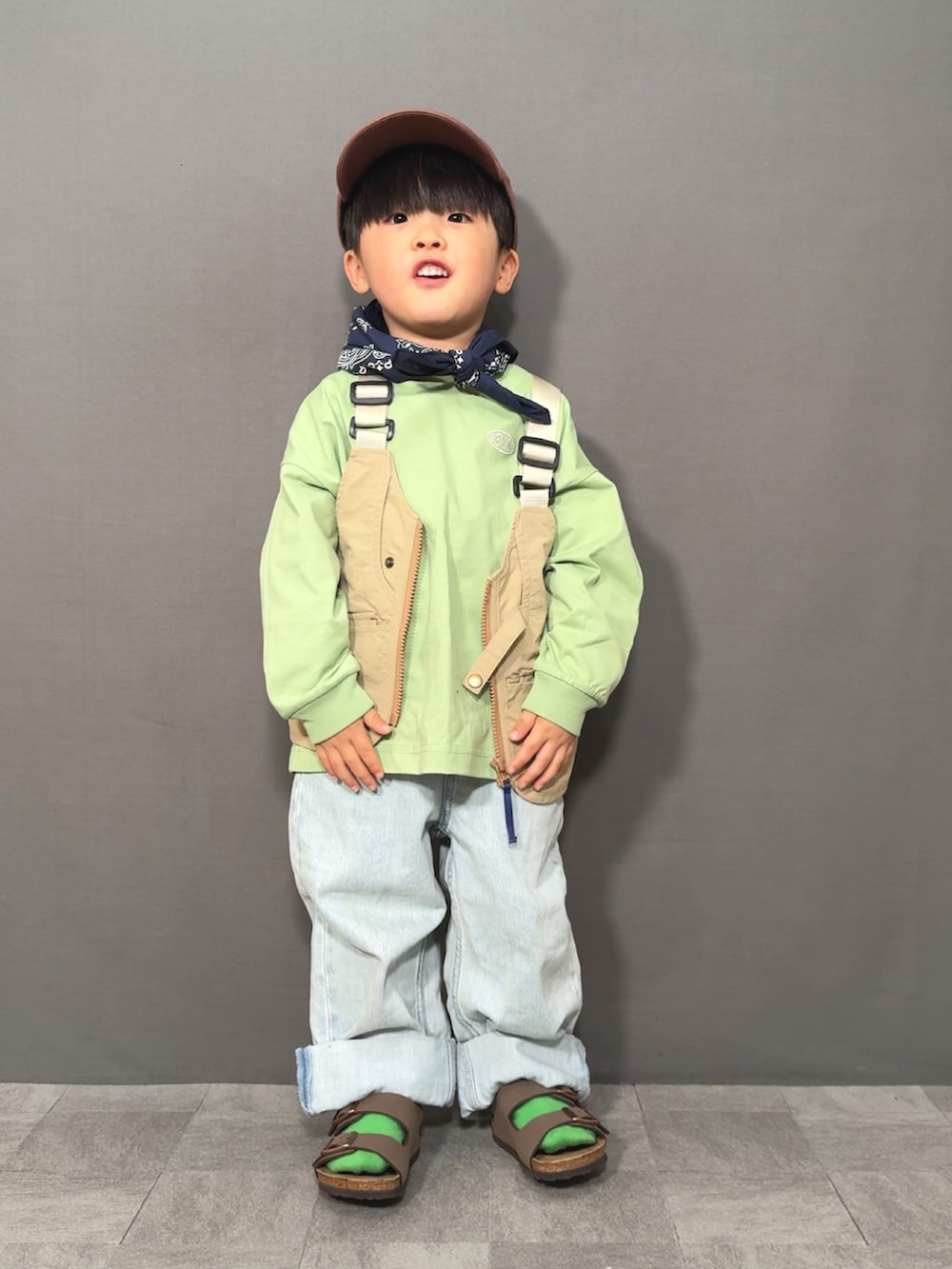 ベージュ系のベスト、グリーン系のTシャツ/カットソー、ブルー系のデニムパンツを着用したキッズの春コーディネートの2枚目の写真