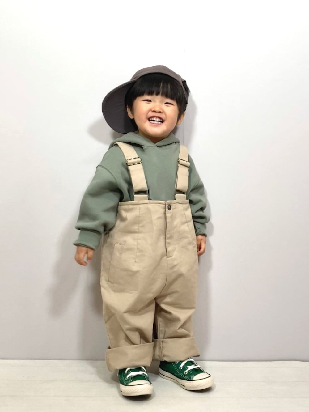 グリーン系のスウェット、ベージュ系のサロペット/オーバーオール、グリーン系のスニーカーを着用したキッズの春コーディネートの2枚目の写真