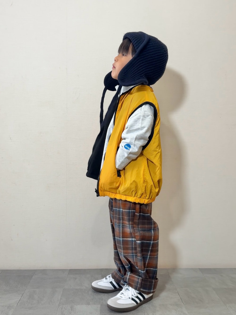 イエロー系のベスト、ホワイト系のスニーカー、グレー系のスウェットを着用したキッズの秋コーディネートの3枚目の写真