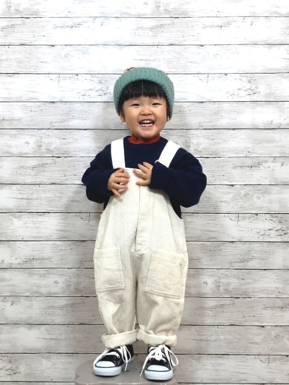 ブルー系のニット/セーター、オレンジ系のTシャツ/カットソー、ベージュ系のサロペット/オーバーオールを着用したキッズの冬コーディネートの2枚目の写真