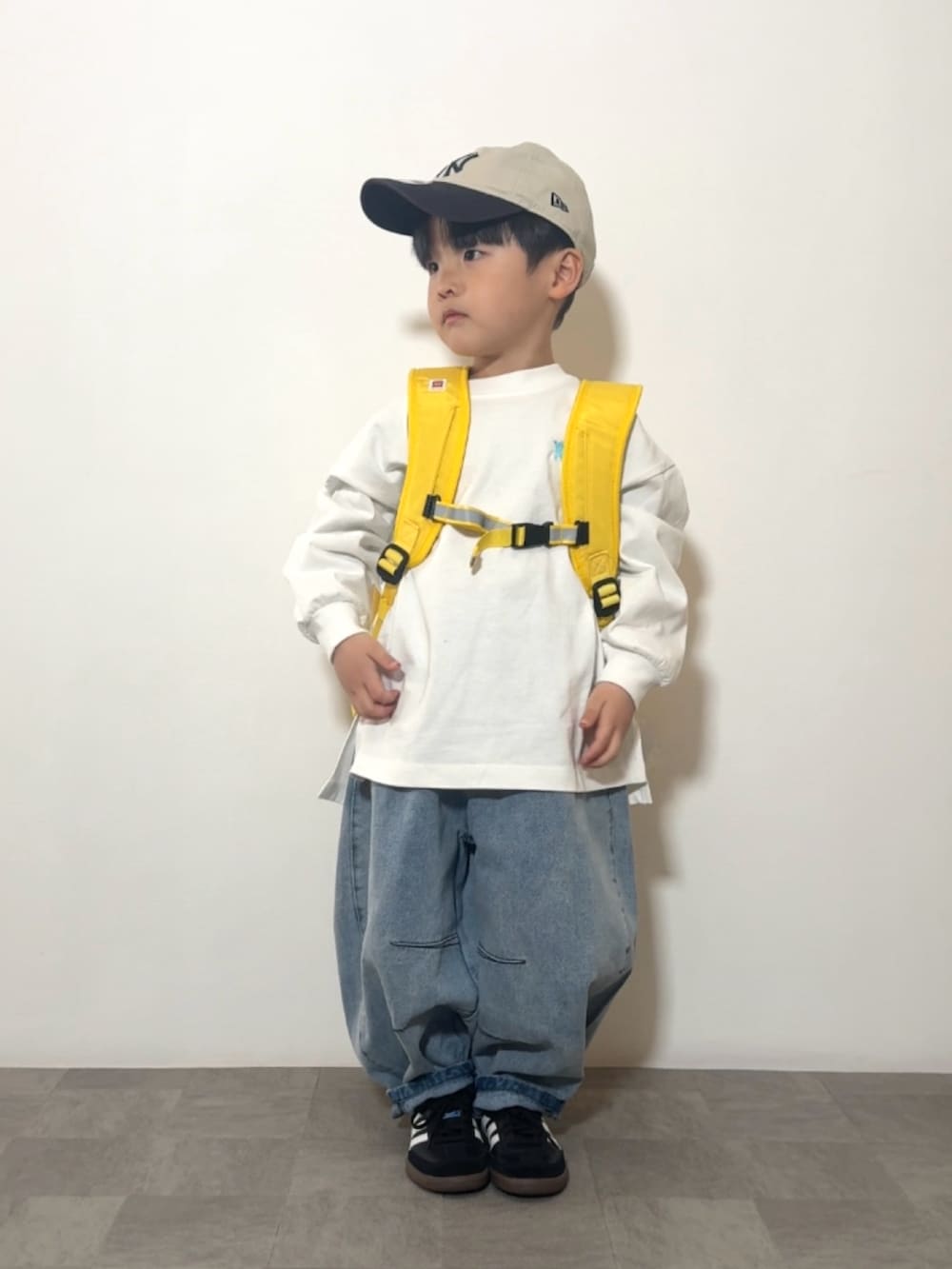 イエロー系のバックパック/リュック、ブラック系のスニーカー、ホワイト系のTシャツ/カットソーを着用したキッズの春コーディネートの2枚目の写真