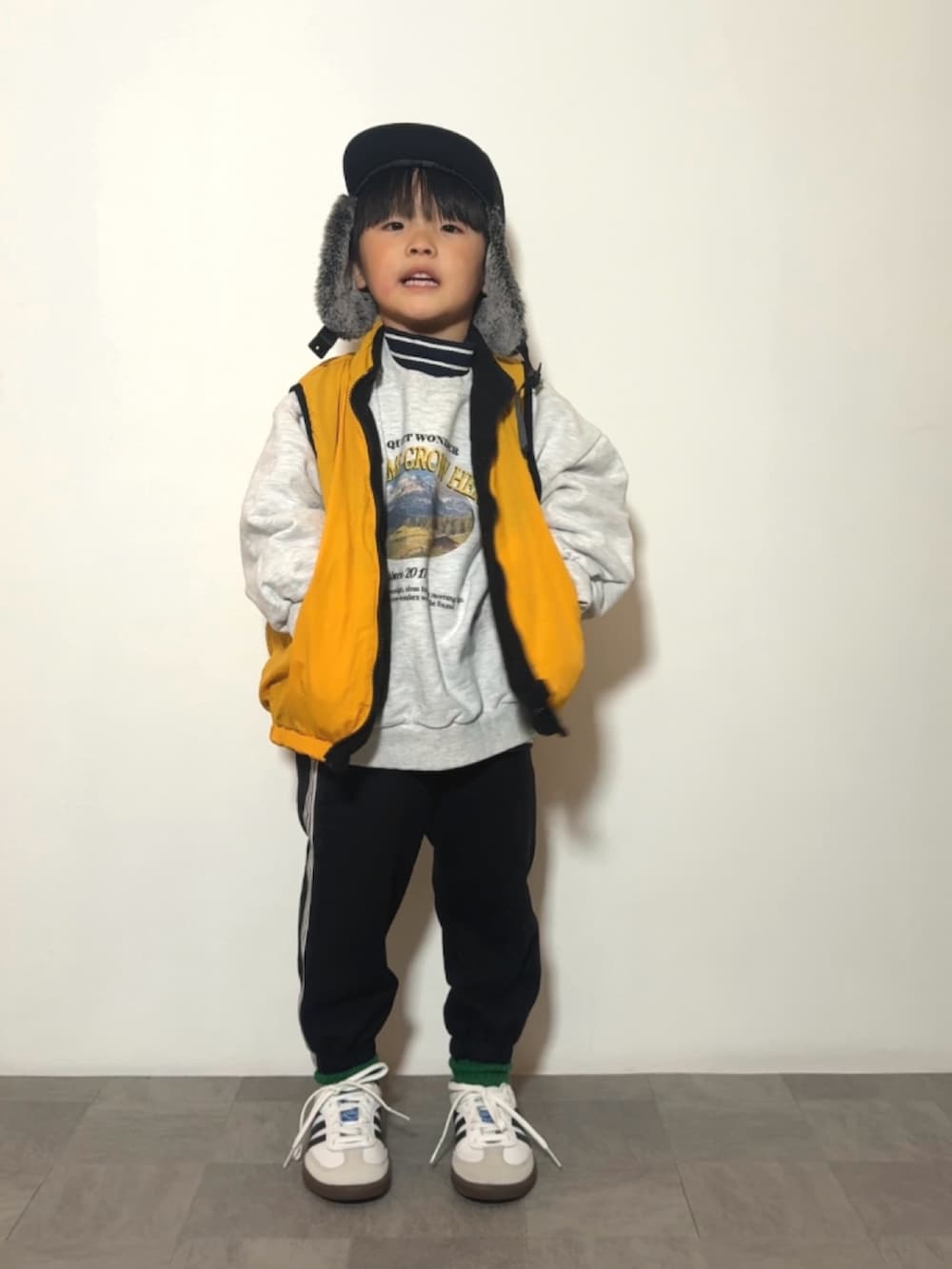 イエロー系のベスト、ブラック系のスウェットパンツ、ホワイト系のスニーカーを着用したキッズの冬コーディネートの3枚目の写真