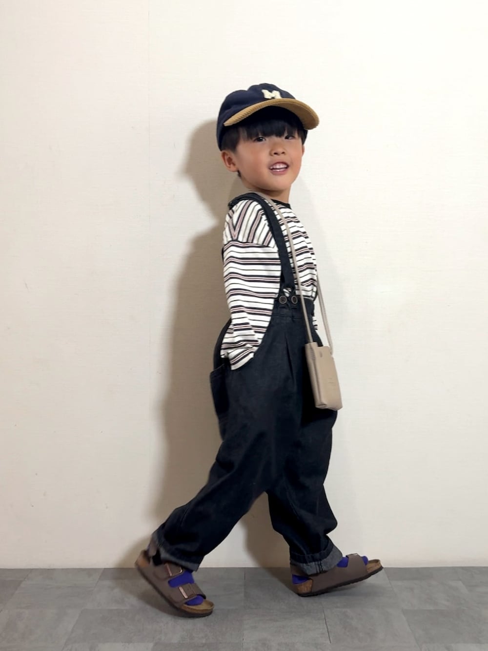 ブラック系のサロペット/オーバーオール、ブラウン系のサンダル、ベージュ系のショルダーバッグを着用したキッズの夏コーディネートの3枚目の写真