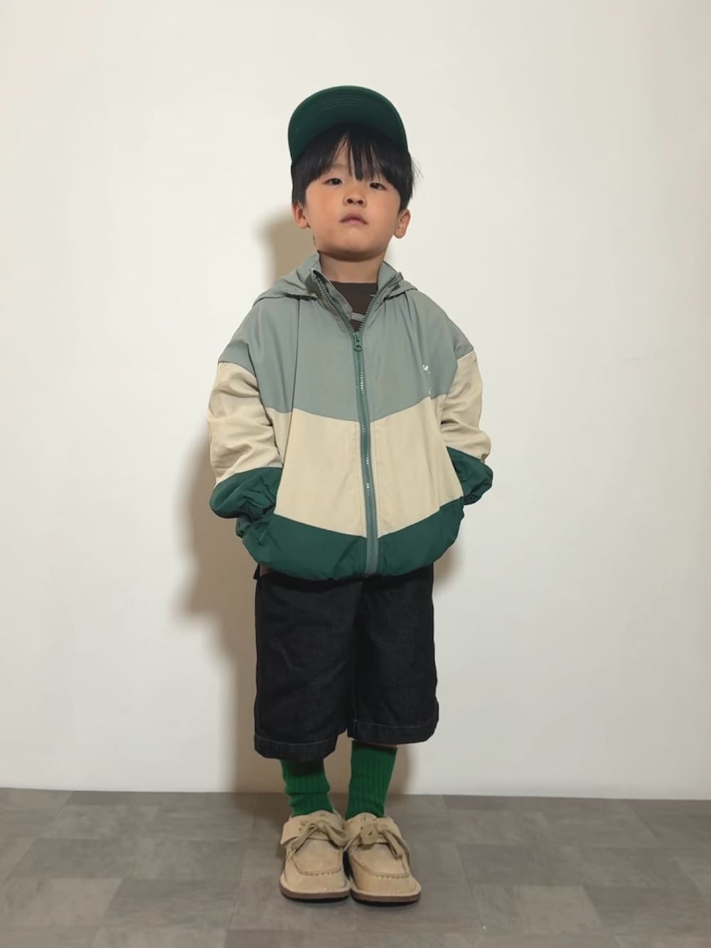 グリーン系のナイロンジャケット、ブラウン系のTシャツ/カットソー、ベージュ系のモカシン/デッキシューズを着用したキッズの冬コーディネートの2枚目の写真