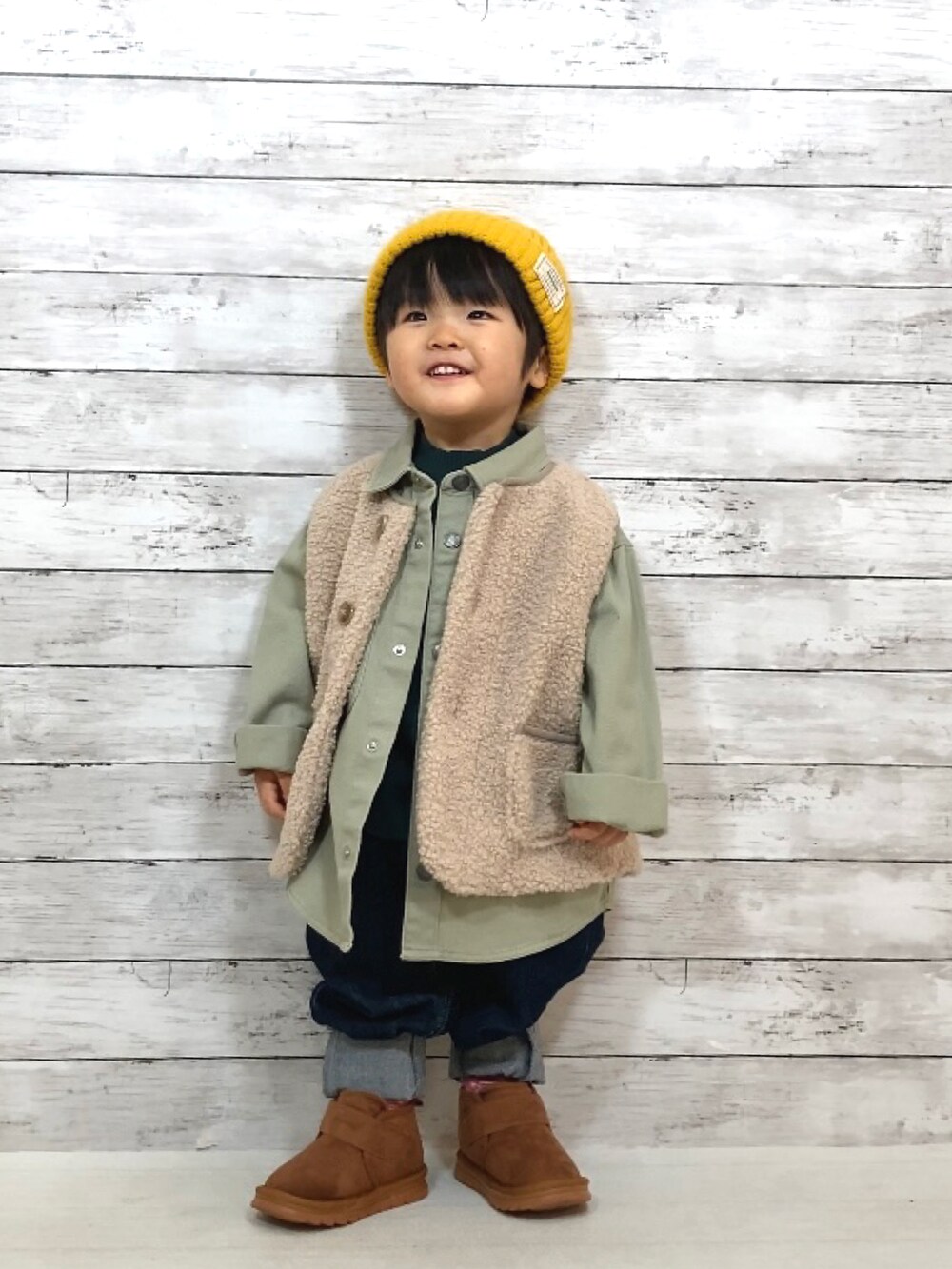 ベージュ系のベスト、グリーン系のTシャツ/カットソー、ブルー系のデニムパンツを着用したキッズの冬コーディネートの2枚目の写真