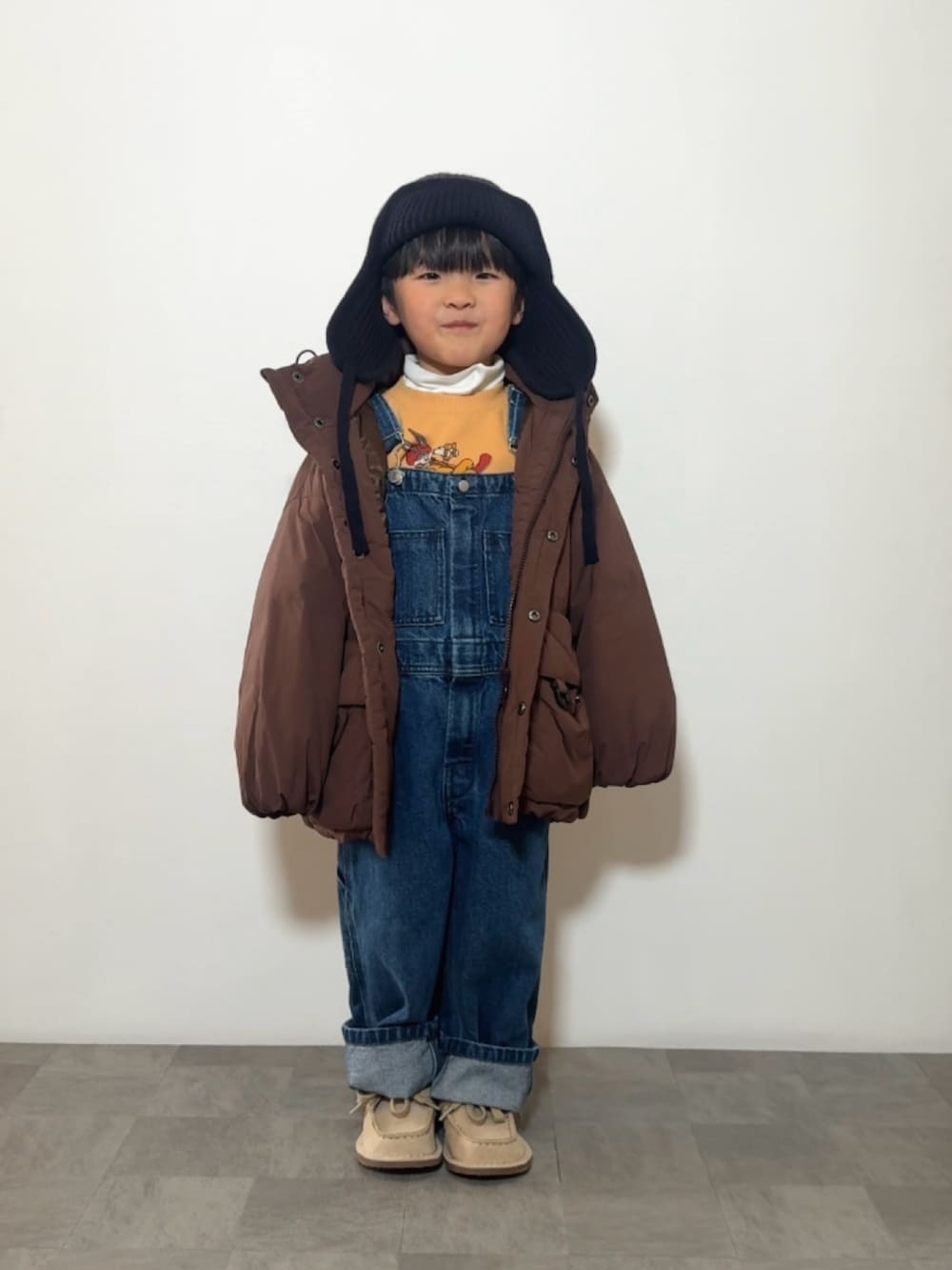 イエロー系のスウェット、ブラウン系のダウンジャケット/コート、ベージュ系のモカシン/デッキシューズを着用したキッズの冬コーディネートの3枚目の写真