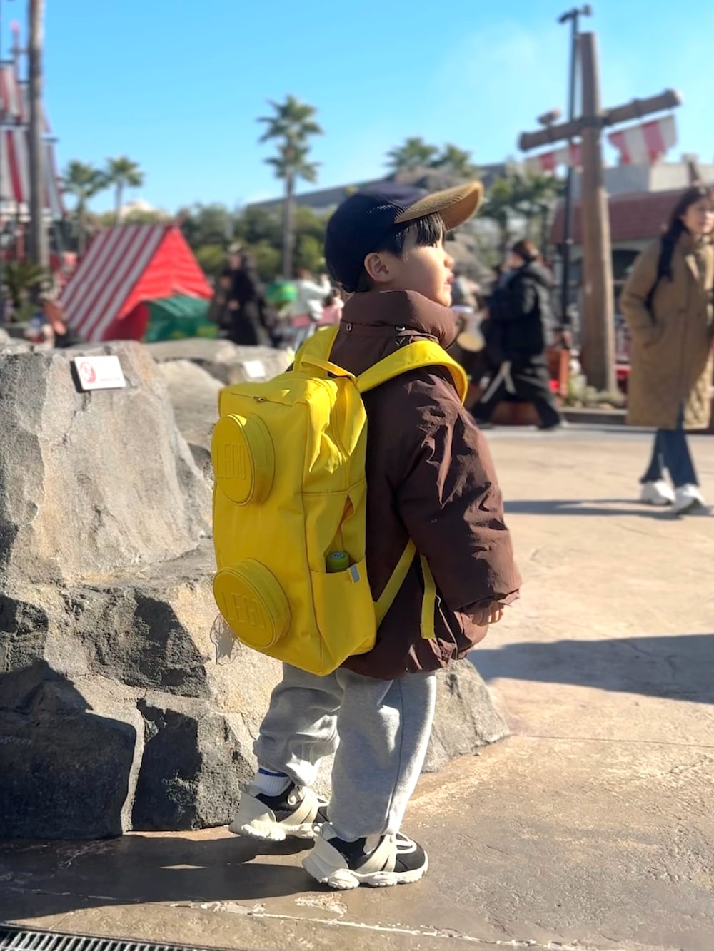 ブラウン系のダウンジャケット/コート、グレー系のスウェットパンツ、イエロー系のバックパック/リュックを着用したキッズの冬コーディネートの2枚目の写真