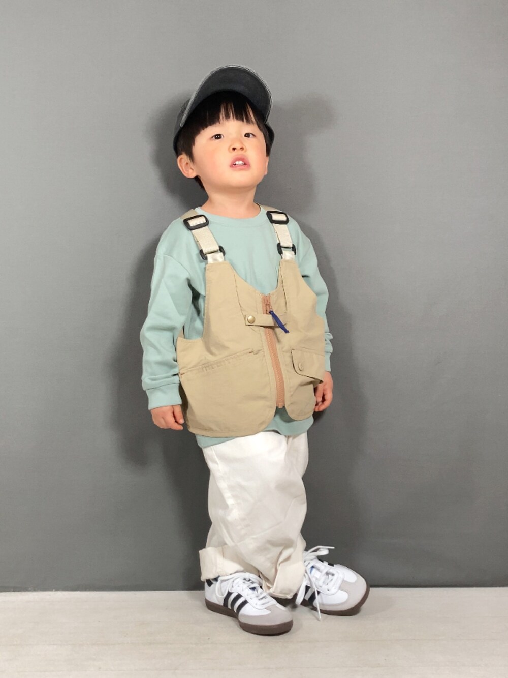 ベージュ系のベスト、グリーン系のTシャツ/カットソー、ホワイト系のパンツを着用したキッズの春コーディネートの2枚目の写真