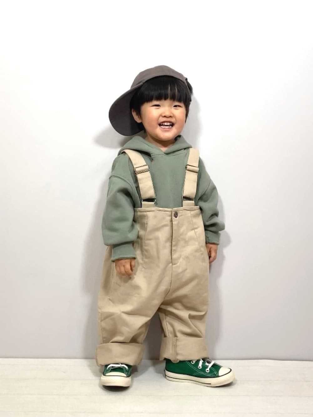 グリーン系のスウェット、ベージュ系のサロペット/オーバーオール、グリーン系のスニーカーを着用したキッズの春コーディネートの3枚目の写真