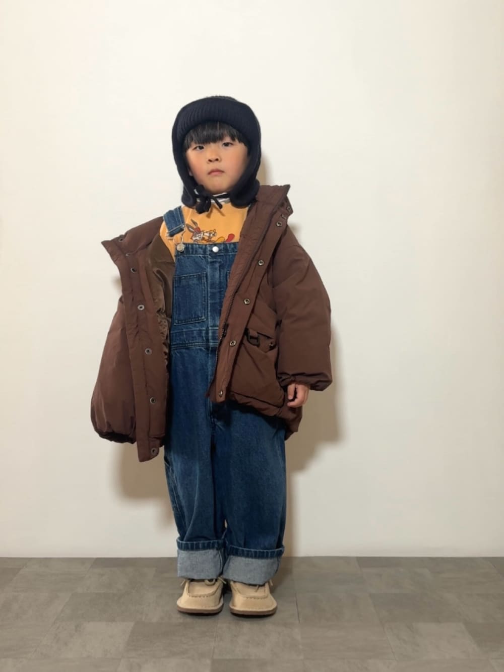 イエロー系のスウェット、ブラウン系のダウンジャケット/コート、ベージュ系のモカシン/デッキシューズを着用したキッズの冬コーディネートの2枚目の写真