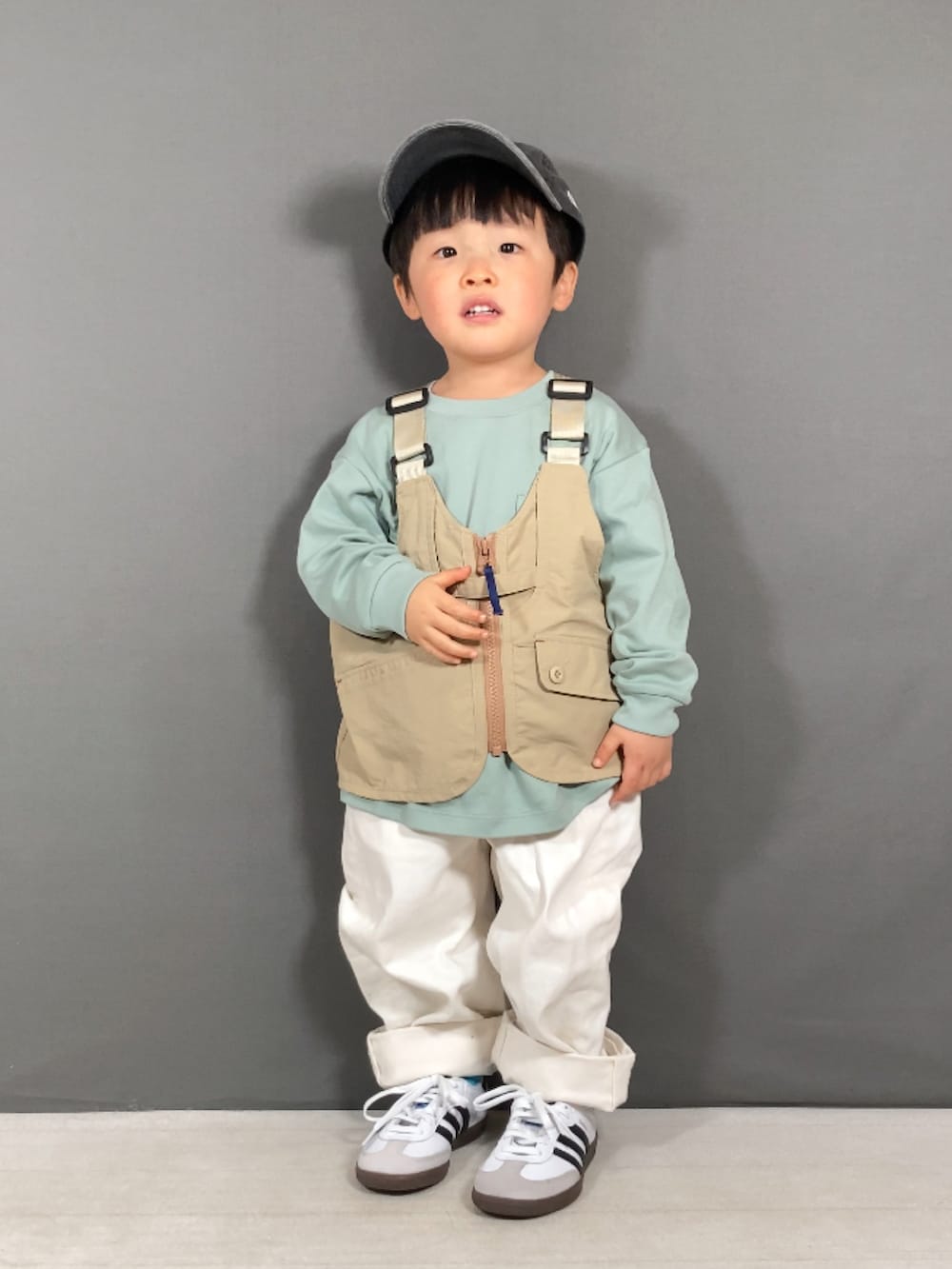 ベージュ系のベスト、グリーン系のTシャツ/カットソー、ホワイト系のパンツを着用したキッズの春コーディネートの3枚目の写真