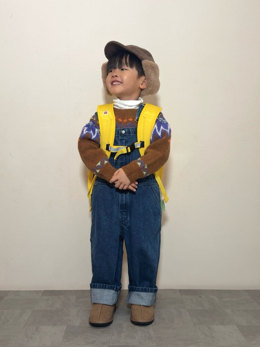 イエロー系のブーツ、イエロー系のバックパック/リュック、ブラウン系のニット/セーターを着用したキッズの冬コーディネートの2枚目の写真