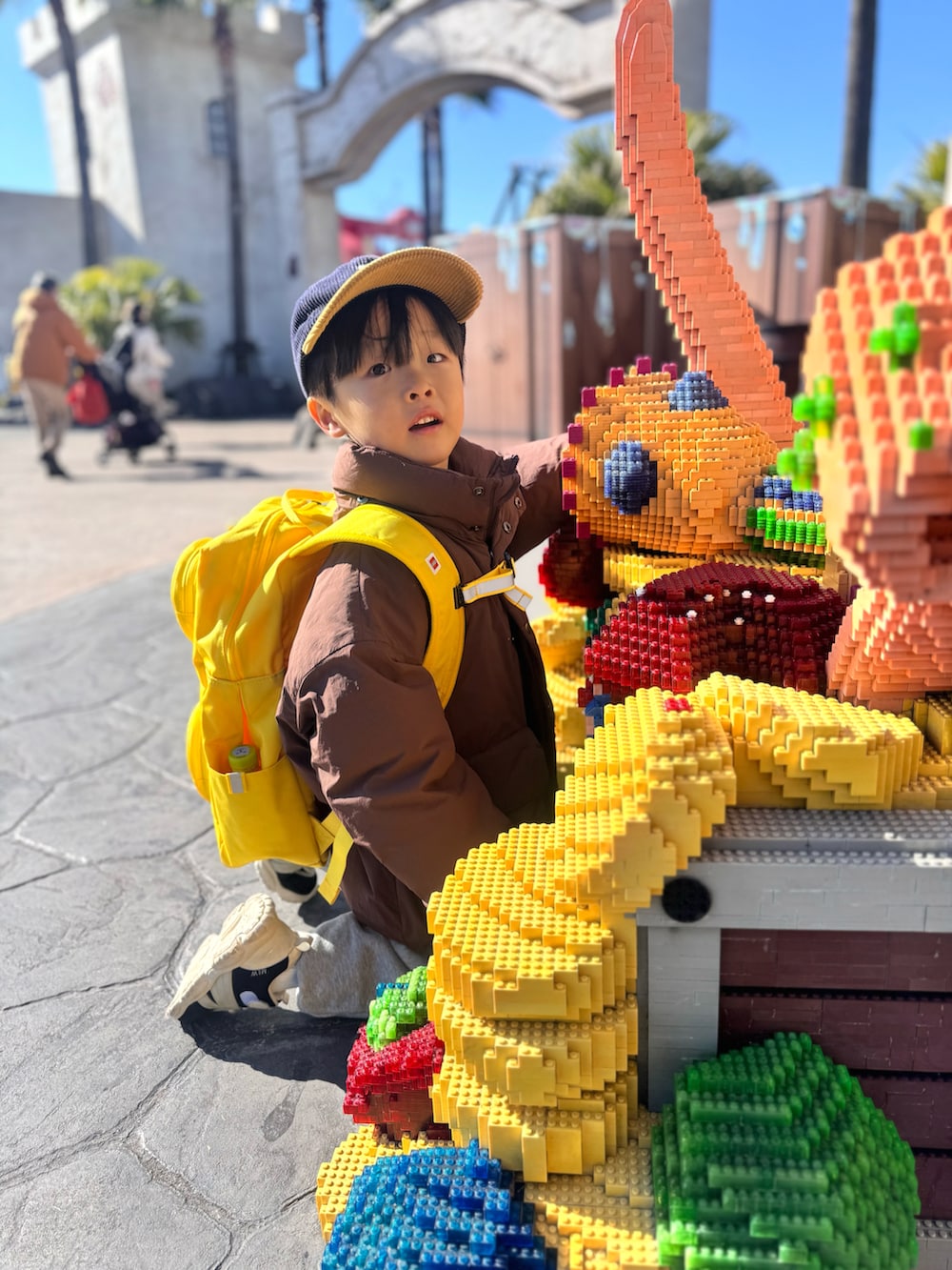 ブラウン系のダウンジャケット/コート、グレー系のスウェットパンツ、イエロー系のバックパック/リュックを着用したキッズの冬コーディネートの5枚目の写真