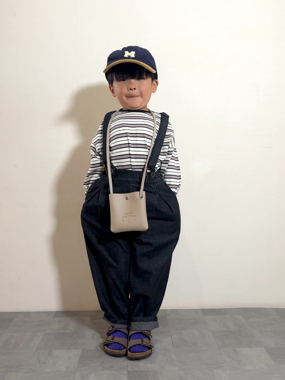 ブラック系のサロペット/オーバーオール、ブラウン系のサンダル、ベージュ系のショルダーバッグを着用したキッズの夏コーディネートの2枚目の写真