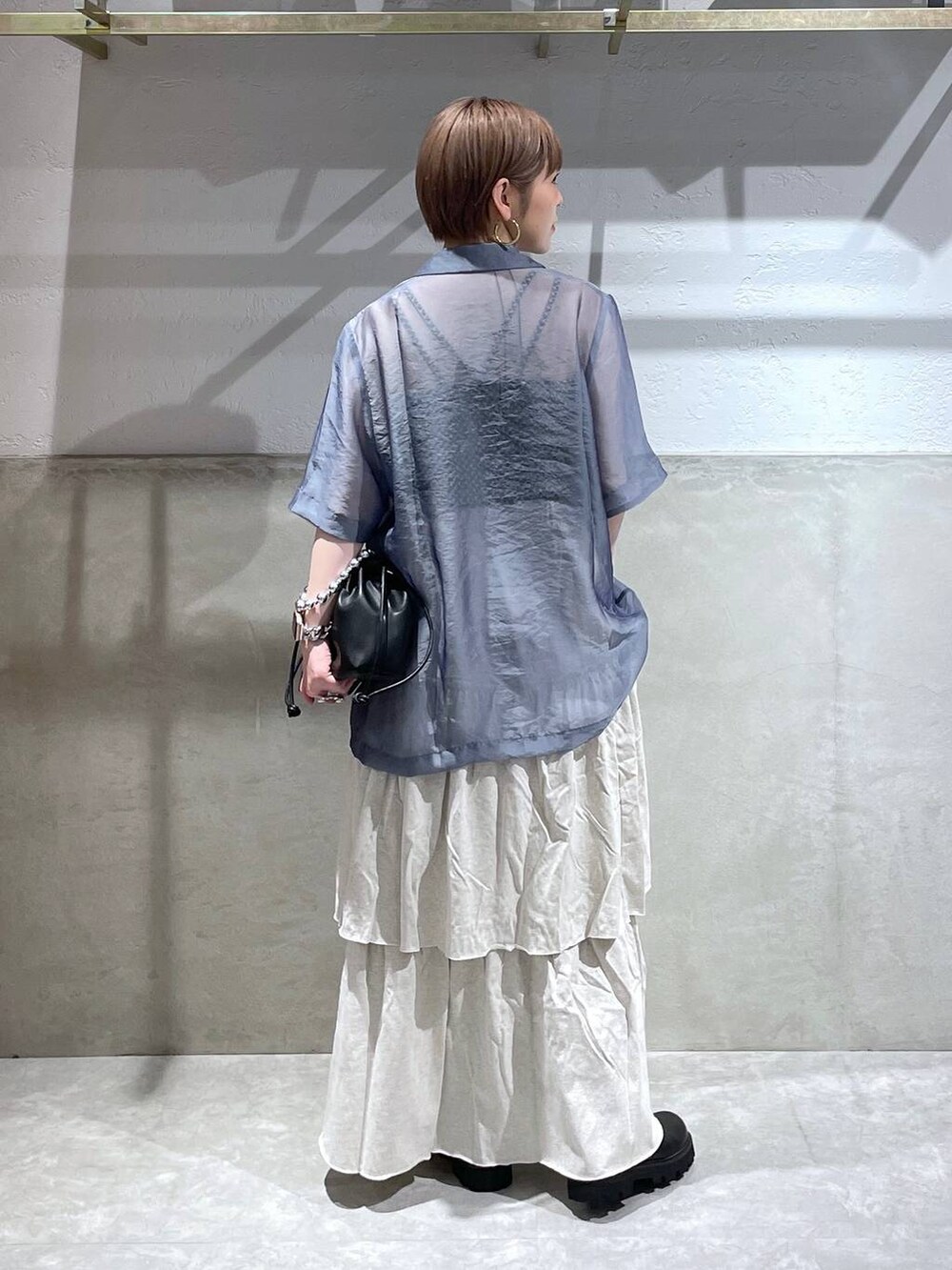 グレー系のスカート、ブラック系のショルダーバッグ、ブラック系のブーツを着用したレディースの夏コーディネートの3枚目の写真