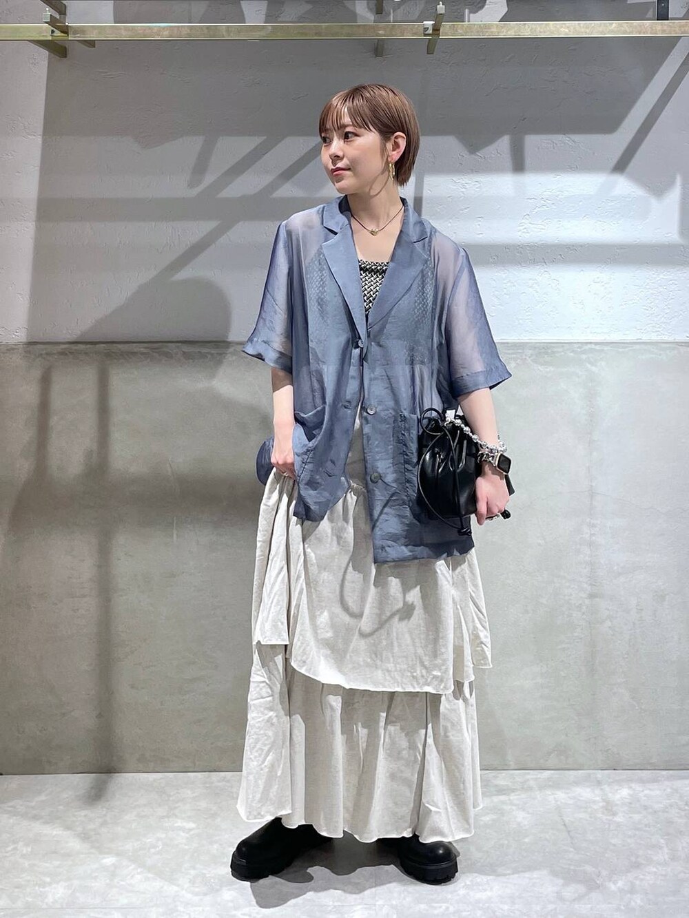 グレー系のスカート、ブラック系のショルダーバッグ、ブラック系のブーツを着用したレディースの夏コーディネートの2枚目の写真