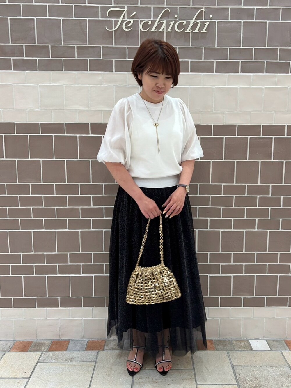 ホワイト系のニット/セーター、ブラック系のスカート、ブラック系のサンダルを着用したレディースの春コーディネートの2枚目の写真