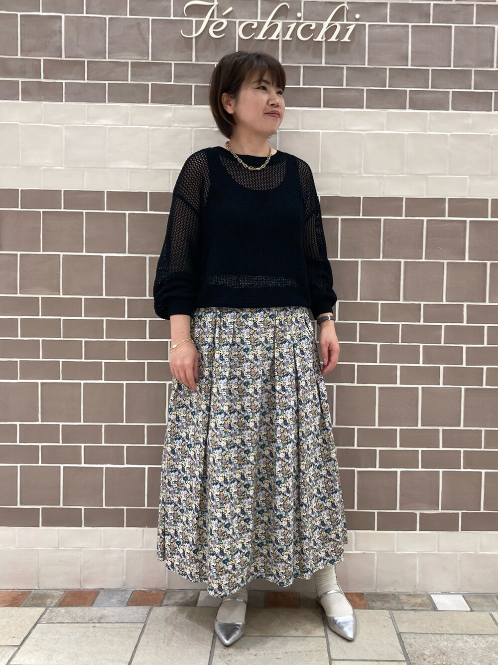 ブラック系のニット/セーター、ブルー系のスカート、シルバー系のパンプスを着用したレディースの春コーディネートの2枚目の写真