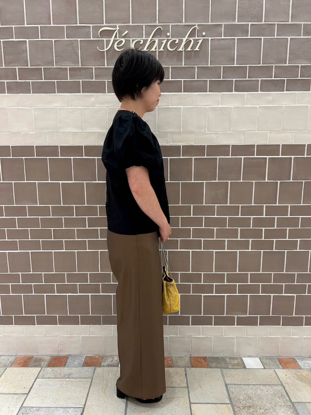 ブラック系のシャツ/ブラウス、ブラウン系のパンツ、ゴールド系のハンドバッグを着用したレディースの夏コーディネートの3枚目の写真