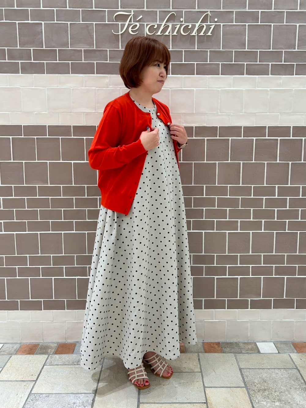 ベージュ系のワンピース/ドレス、レッド系のカーディガン/ボレロ、ホワイト系のサンダルを着用したレディースの夏コーディネートの3枚目の写真