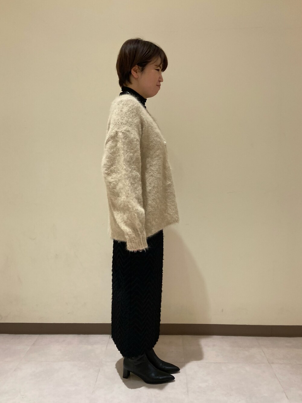 ベージュ系のカーディガン/ボレロ、ブラック系のスカート、ブラック系のブーツを着用したレディースの冬コーディネートの2枚目の写真